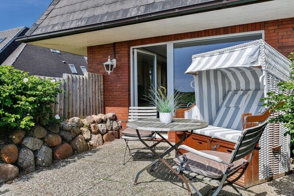 A patio with a round table and chairs, a potted plant, and a striped awning. - House section Heideblick (Kampen)
