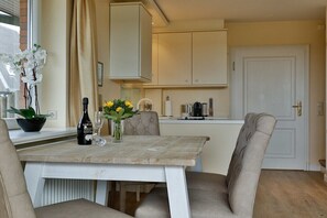 A dining area with a table, chairs, a vase with flowers, a bottle, and a coffee machine. - House section Heideblick (Kampen)