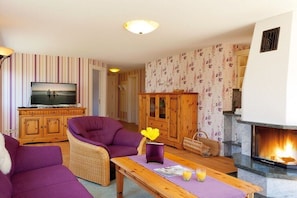 A living room with a television, purple sofas, a wooden cabinet, a fireplace, and a patterned wall. - Holiday apartment with 1 bedroom (Usedom)
