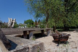 Un espace extérieur rustique agrémenté d’un pont en bois, d’un foyer rustique et d’un grand arbre.