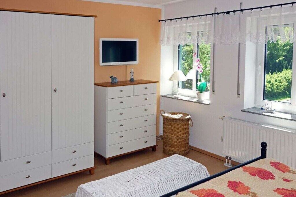 Une chambre à coucher comprenant un lit, une armoire, un téléviseur, une fenêtre avec des rideaux et un radiateur.