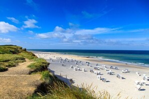 Een strand met rijen witte ligbedden en een helderblauwe lucht.