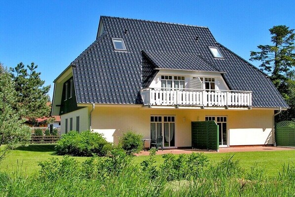 Een woonhuis met twee verdiepingen, een schuin dak, een balkon en een voordeur.