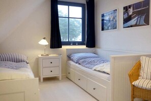 Een slaapkamer met raam, nachtkastje met lamp, bed met gestreept beddengoed, en een stoel.