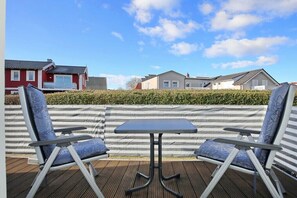 Un patio al aire libre con una mesa y dos sillas, una terraza de madera y un seto al fondo.