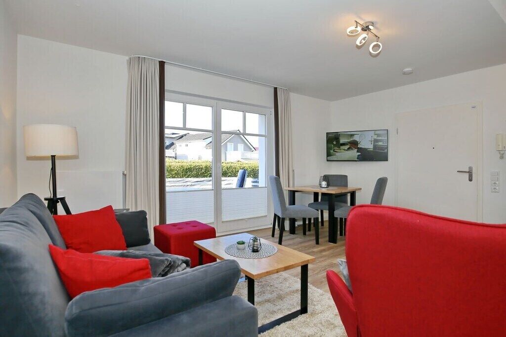 Un salon moderne avec un canapé, des fauteuils rouges et gris, une petite table et un coin repas comprenant des chaises et une table.