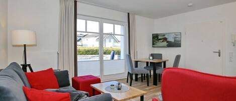 A modern living room with a sofa, red and grey chairs, a small table, and a dining area with chairs and a table.