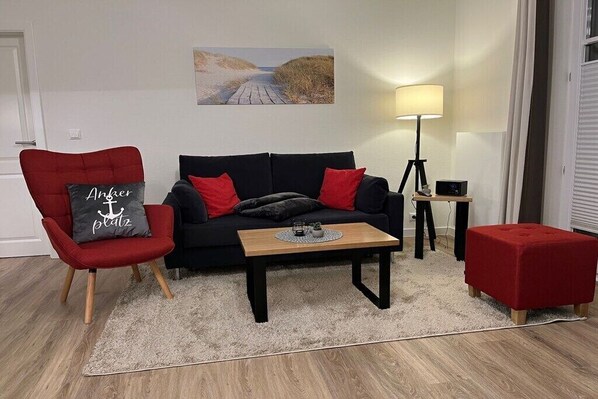 Una sala de estar con un sofá negro, un sillón rojo y una pequeña mesa con una lámpara.