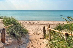 Een zandstrand met een houten omheining en gras op de voorgrond.