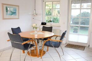 Een eetruimte met een ronde tafel, vier gestreept stoelen, een vaas met bloemen, een ingelijst kunstwerk aan de muur en een raam met uitzicht op groen.