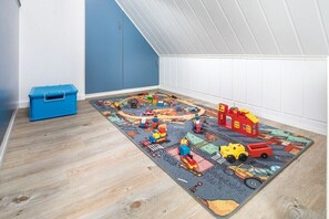 Ein Zimmer mit einer Spieleunterlage, Spielzeugautos und -gebäuden, einer blauen Aufbewahrungsbox und einer schrägen Decke.