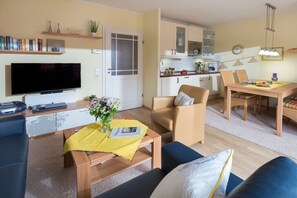 A living room with a TV, sofa, coffee table, and a dining area with a table and chairs. - Seagull's Nest Südwesthörn 9c (Norderney)