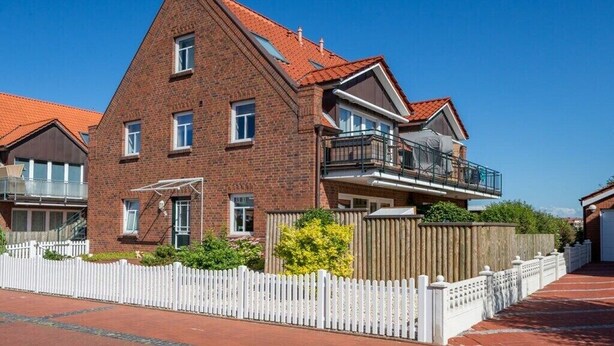 Ein zweistöckiges Ziegelhaus mit Balkon und weißem Zaun, bewölkter, klarer Himmel.