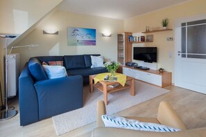 A modern living room with a sofa, coffee table, and TV. - Seagull's Nest Südwesthörn 9c (Norderney)