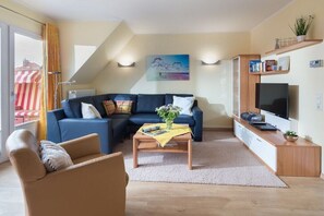 A modern living room with a sectional sofa, a coffee table, a TV, and a bookshelf. - Seagull's Nest Südwesthörn 9c (Norderney)