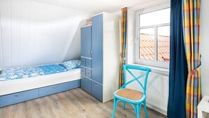 Ein Schlafzimmer mit einem Bett, einem Kleiderschrank, einem Sessel und einem Fenster.