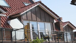 Ein Wohngebäude mit geneigtem Dach, großen Fenstern und einem Balkon mit Geländern.