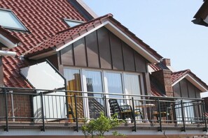 Un edificio residencial con techo inclinado, ventanas amplias y un balcón con barandillas.
