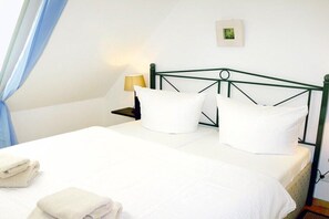 Een netjes opgemaakt bed met witte lakens en kussens, een bedlampje en een lijst met een foto aan de muur.
