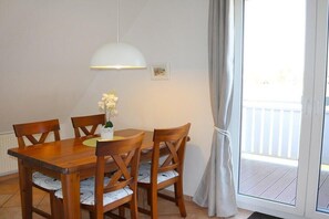Een eetgedeelte met een houten tafel en stoelen, een hanglamp en uitzicht op een balkon door een glazen deur.