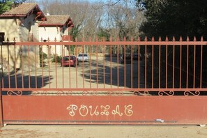 A gated entrance with a metal fence and a building with a tiled roof in the background. - Gîte Les Vendangeurs (Servian)