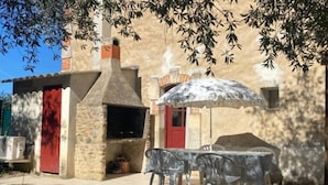 Un patio esterno con un camino in pietra, una porta rossa e un tavolo con sedie.