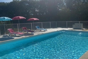 Een zwembad met helderblauw water, omringd door een metalen hek, en voorzien van meerdere ligbedden en parasols.