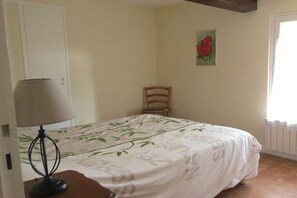 A bedroom with a bed, a chair, a lamp, and a painting on the wall. - Gîte Les Vendangeurs (Servian)