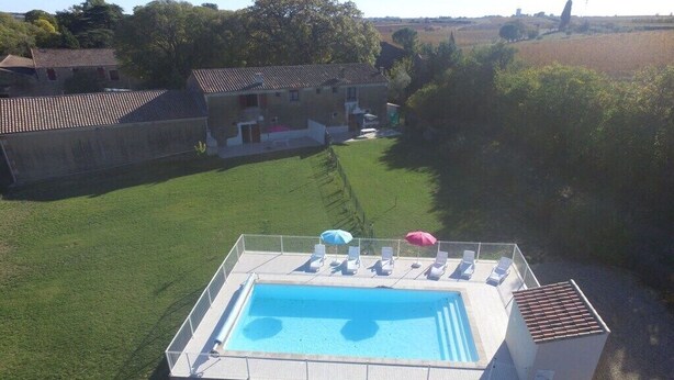 Una piscina con lettini e ombrelloni, circondata da un'area recintata con prato e un edificio sullo sfondo.