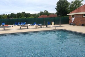 A swimming pool with blue lounge chairs and a brick building in the background. - Holiday home with 3 bedrooms (BX Herkingen)