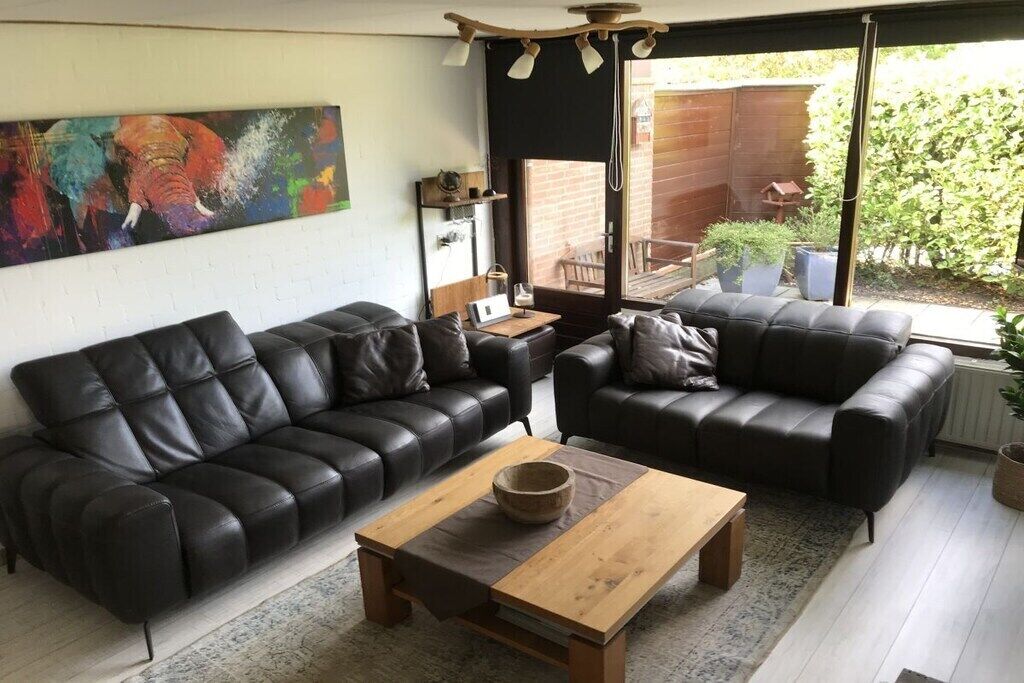 A living room with two black leather sofas, a wooden coffee table, and a colorful abstract painting on the wall.