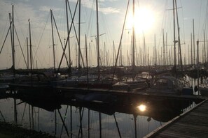 Ein Yachthafen mit mehreren vor Anker liegenden Booten, eine Holzstele und ein Sonnenuntergang im Hintergrund.