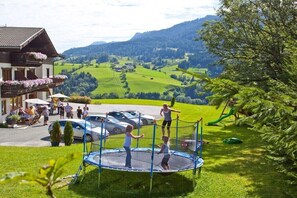 Un quartier résidentiel avec un trampoline installé dans une cour verdoyante, un immeuble doté d’un balcon et une vue panoramique sur une vallée.