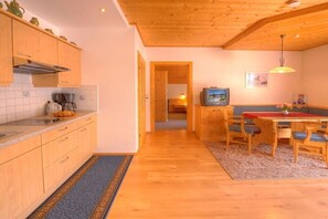 Een keuken met houten kastjes, een eethoek met een tafel en stoelen, en een televisie.