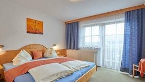 Quarto com cama de madeira, mesa de cabeceira, janela com cortinas e um quadro na parede.
