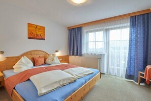 Een slaapkamer met een houten bed, een nachtkastje, een raam met gordijnen en een schilderij aan de muur.