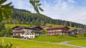 Um hotel com vários edifícios, área de estacionamento e uma estrada serpenteando por uma paisagem verde com colinas ao fundo.