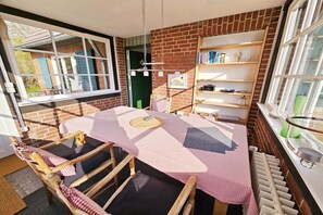A cozy room with a brick wall, a window, a table with a checkered tablecloth, and a bookshelf. - Holiday home with 2 bedrooms (Sierksdorf)