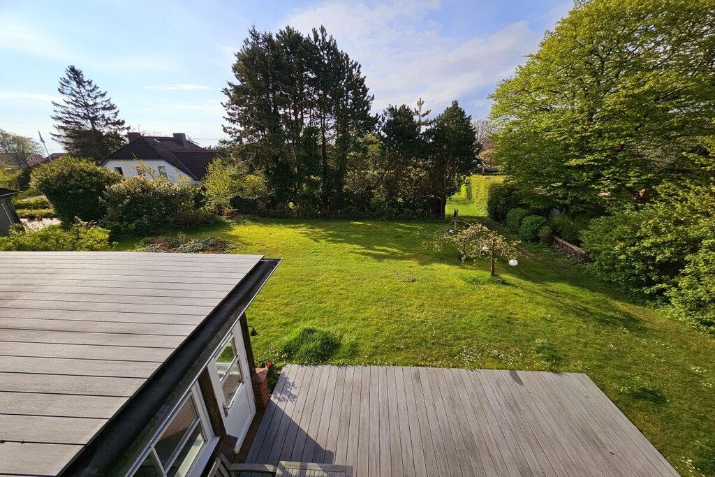 A residential property with a wooden deck, a well-maintained lawn, and surrounding trees.