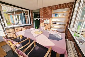 A cozy room with a brick wall, a window, a table with a checkered tablecloth, and a bookshelf. - Holiday home with 2 bedrooms (Sierksdorf)