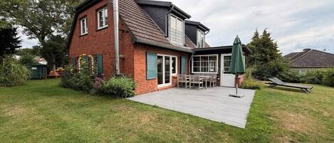 Una casa de dos pisos con fachada de ladrillo, una terraza de madera y un patio con mobiliario exterior.