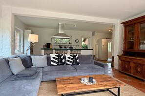 A living room with a grey sofa, a wooden coffee table, and a kitchen area with a stove and cabinets. - Holiday home with 2 bedrooms (Sierksdorf)