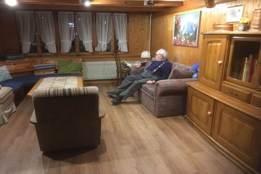 Ein gemütliches Wohnzimmer mit Holzboden, einer Couch, einem Sessel und einem Schrank.