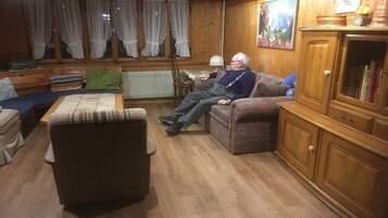 Ein gemütliches Wohnzimmer mit Holzboden, einer Couch, einem Sessel und einem Schrank.
