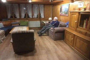 Een gezellige woonkamer met een houten vloer, een bank, een fauteuil en een kast.