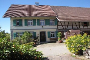 A two-story house with a tiled roof, a front porch, and a sign that reads 'Bio-Anbau.' - Bioland farm Teufelsberg (Horgenzell)