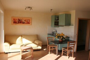 Un espacio habitable compacto con sofá, mesa de comedor, sillas y una zona de cocina con armarios y microondas.