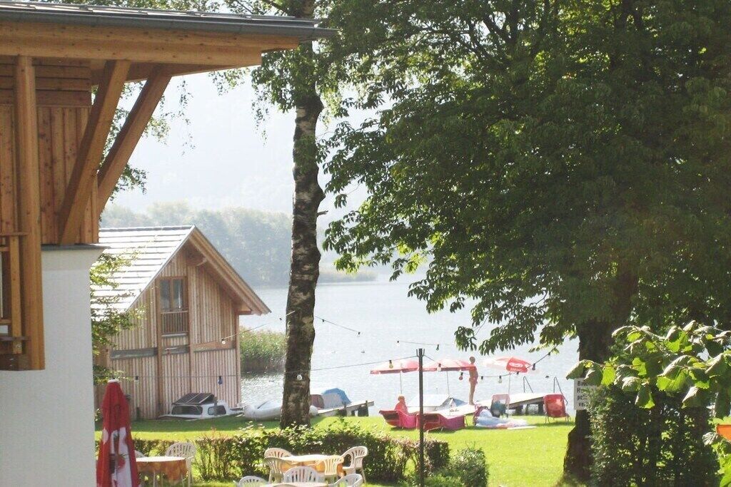 A wooden cabin with a view of a lake, outdoor seating, and boats.