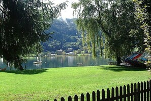 Blick auf einen See mit einer Wiese, einem Holenzaun und Booten.