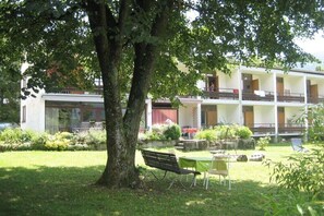 A building with a two-story structure, a grassy courtyard, and a tree providing shade. - Holiday apartment with 2 bedrooms (Steindorf)